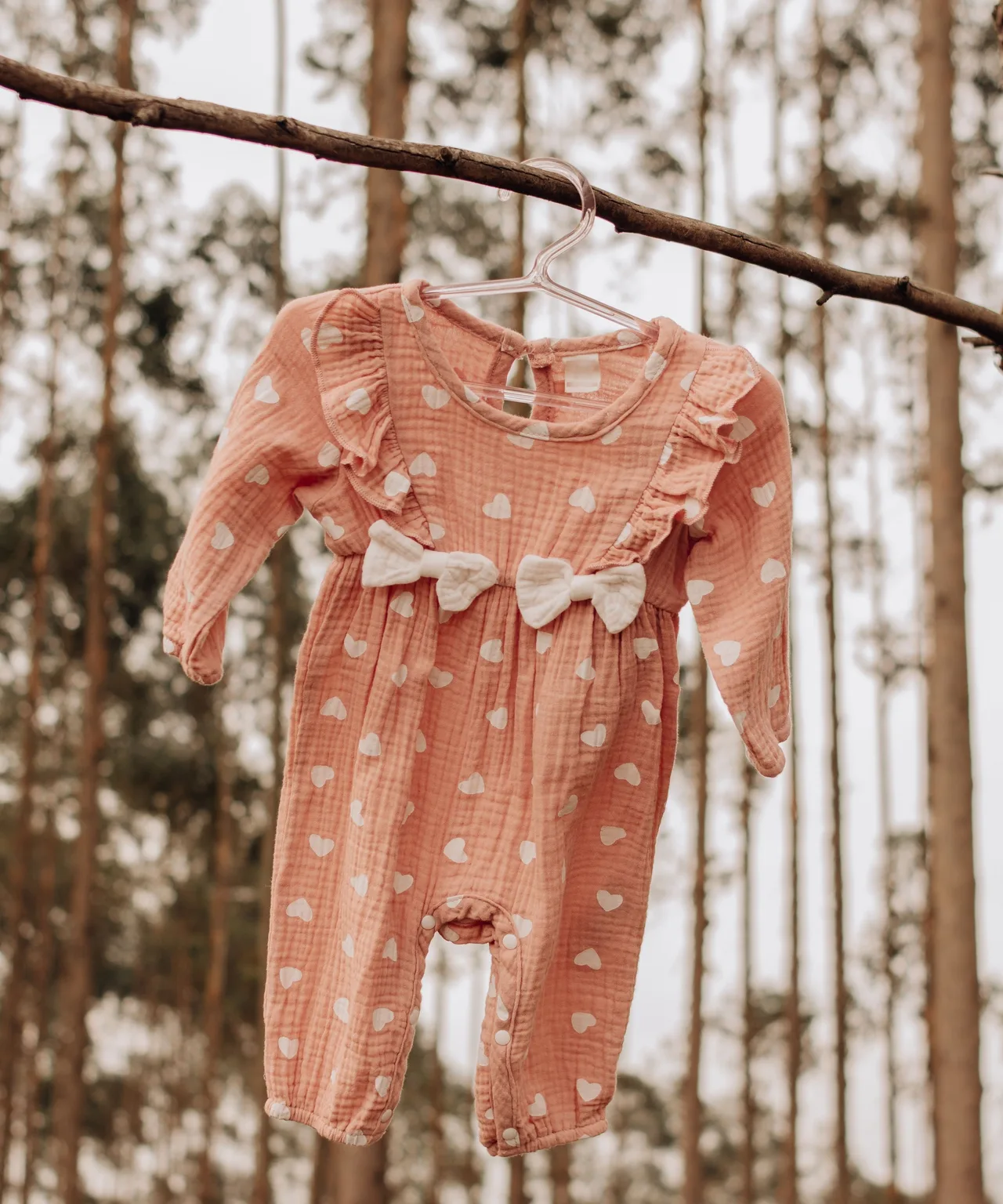 Jumpsuit bayi warna persik dengan dua pita, tergantung di dahan di tengah hutan