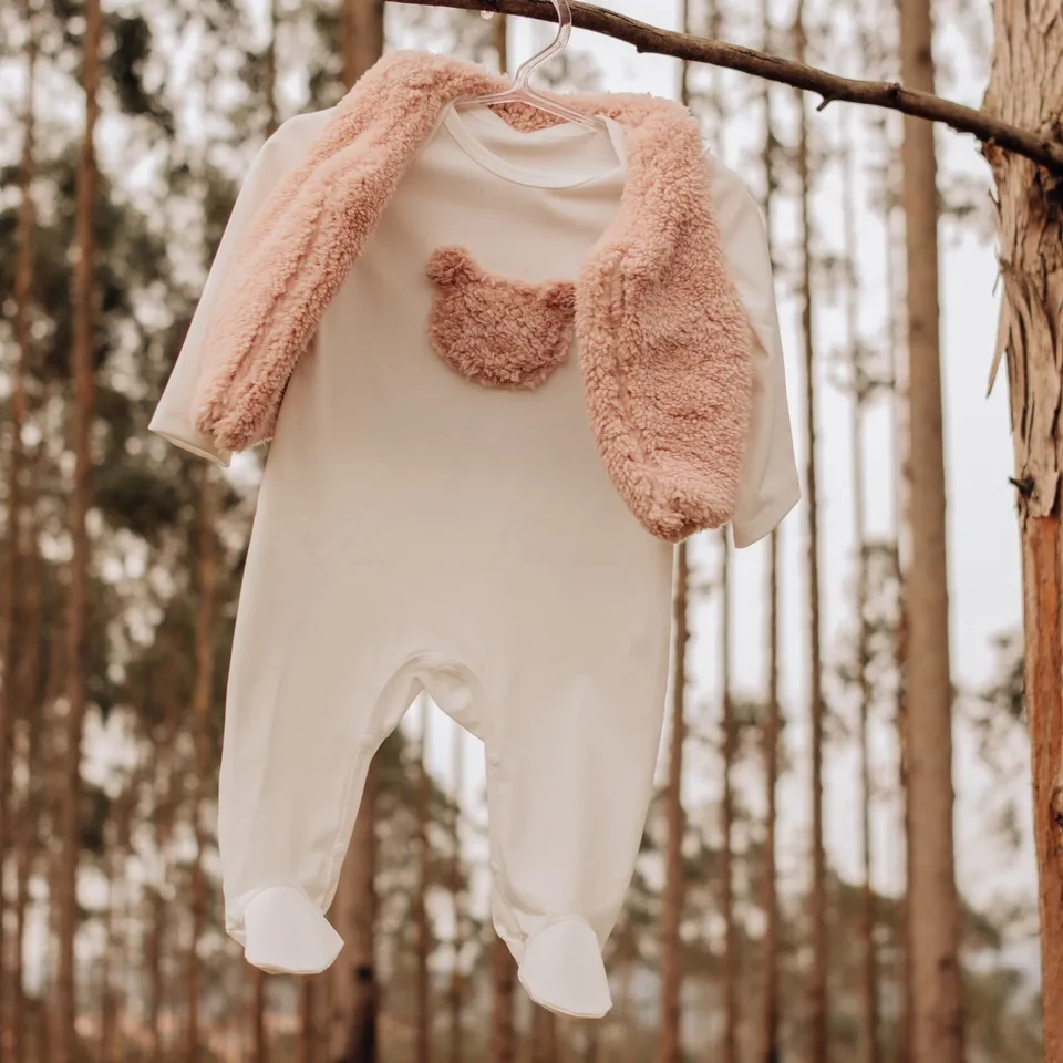Jumpsuit tidur bayi warna krem dengan beruang di dada dan kardigan bulu merah muda, di gantungan