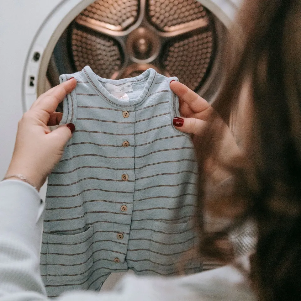 Romper bayi tanpa lengan warna biru abu bergaris, dipegang dengan dua tangan