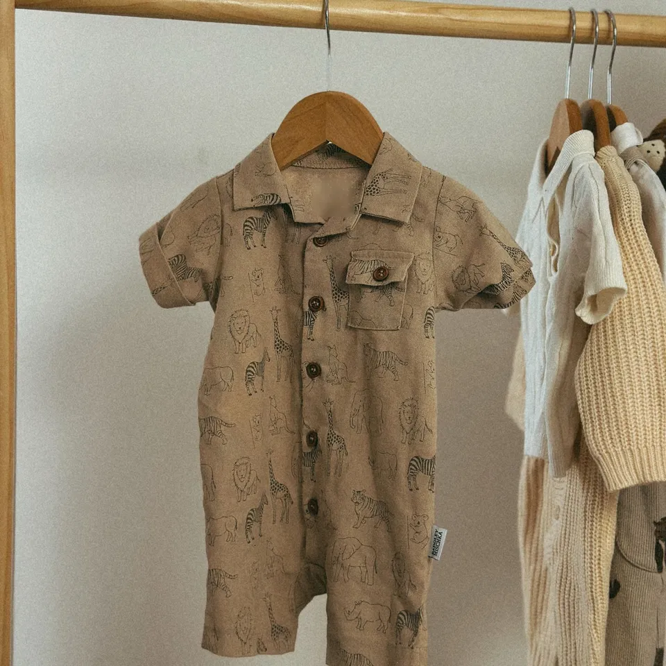 Romper bayi berkerah warna khaki bergambar satwa, tergantung di gantungan kayu
